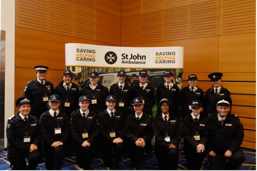 St John Ambulance Ireland Cadets and Leaders in front of a stanf with the words Saving Helping Caring and the St John Ambulance logo. 